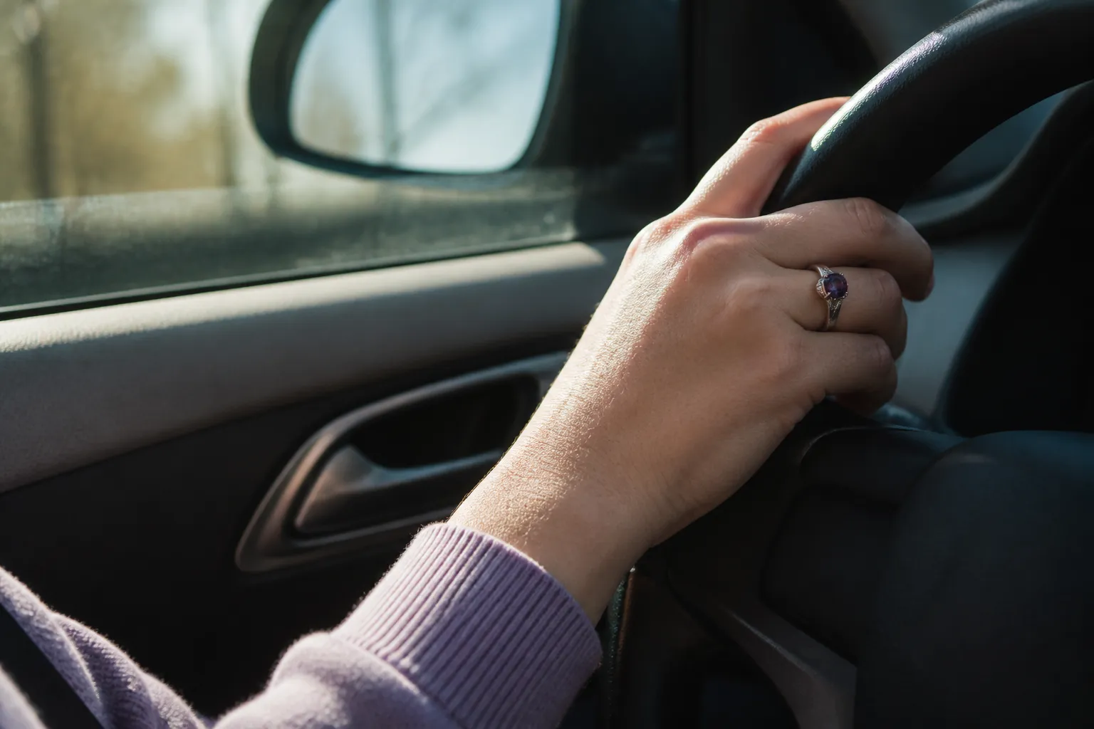 Amethyst ring on the driver-side hand near a car window during a commute
